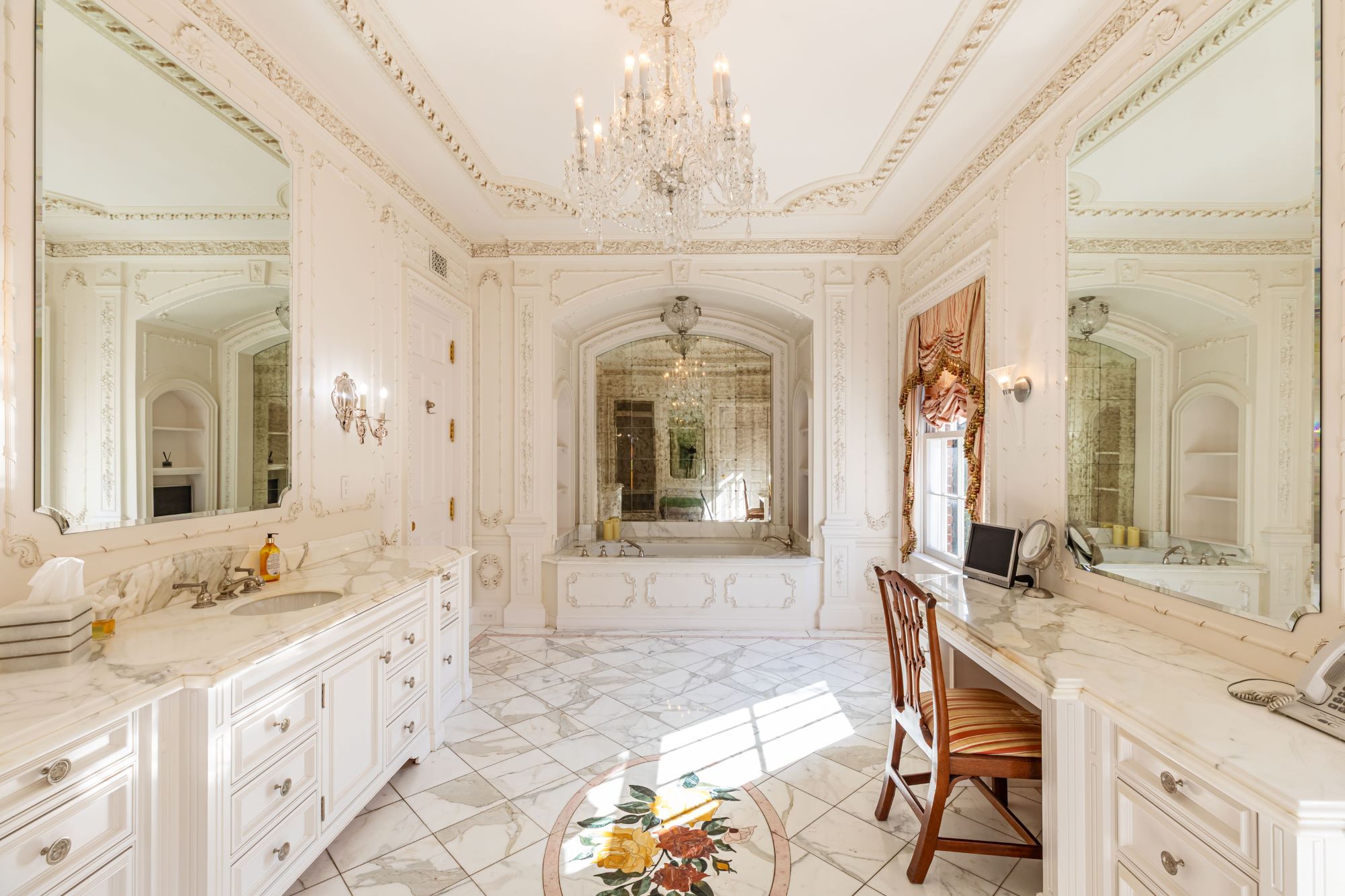 Luxurious bathroom featuring marble countertops, elegant mirrors, a chandelier, and a decorative floor pattern.