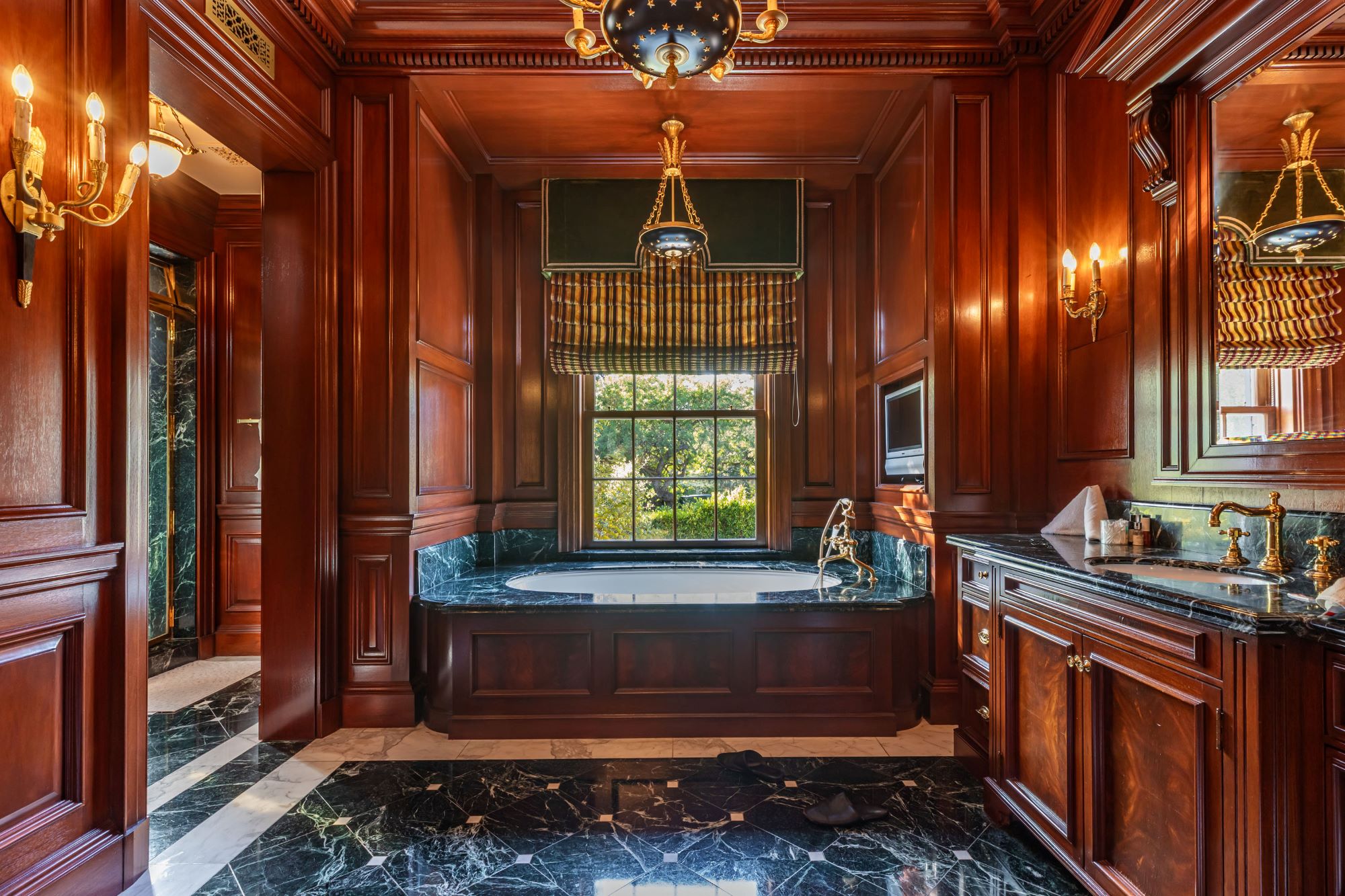 Luxurious bathroom featuring rich wooden paneling, marble flooring, and a soaking tub with a view through elegant windows.