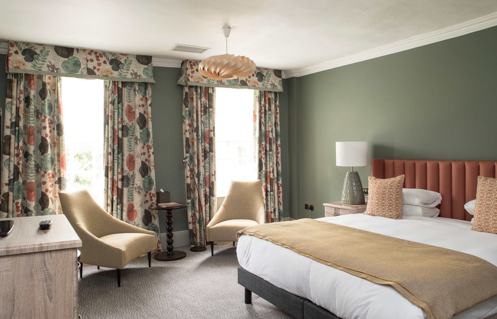 Stylish hotel room featuring a double bed, modern decor, and floral curtains, creating a welcoming atmosphere.