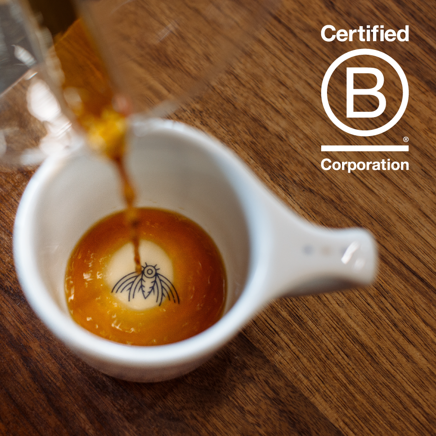 A close-up of brewed coffee pouring into a white cup, featuring an artistic logo design at the bottom.